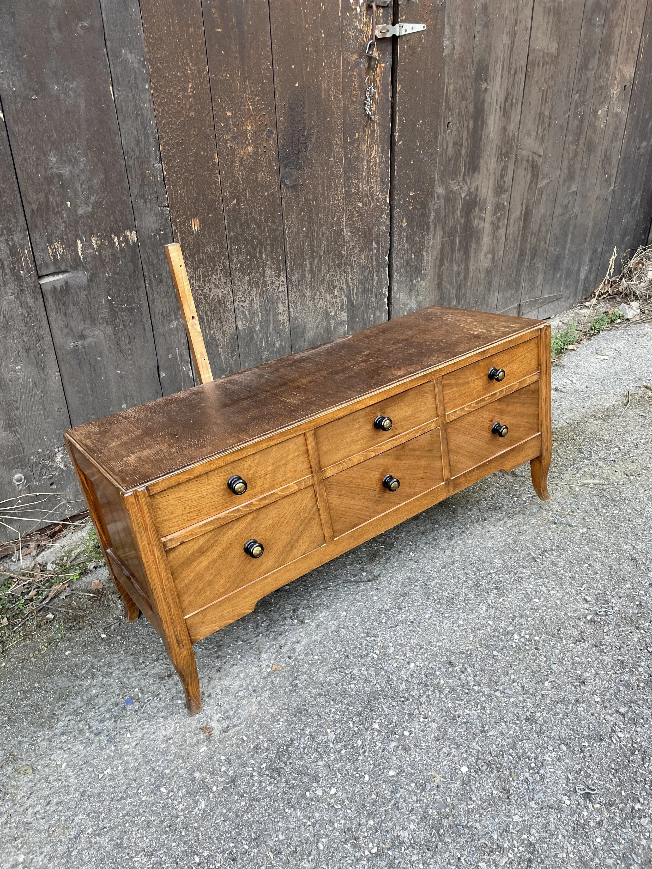 Meuble en bois avec six tiroirs noirs, placé à l'extérieur contre un mur en bois.