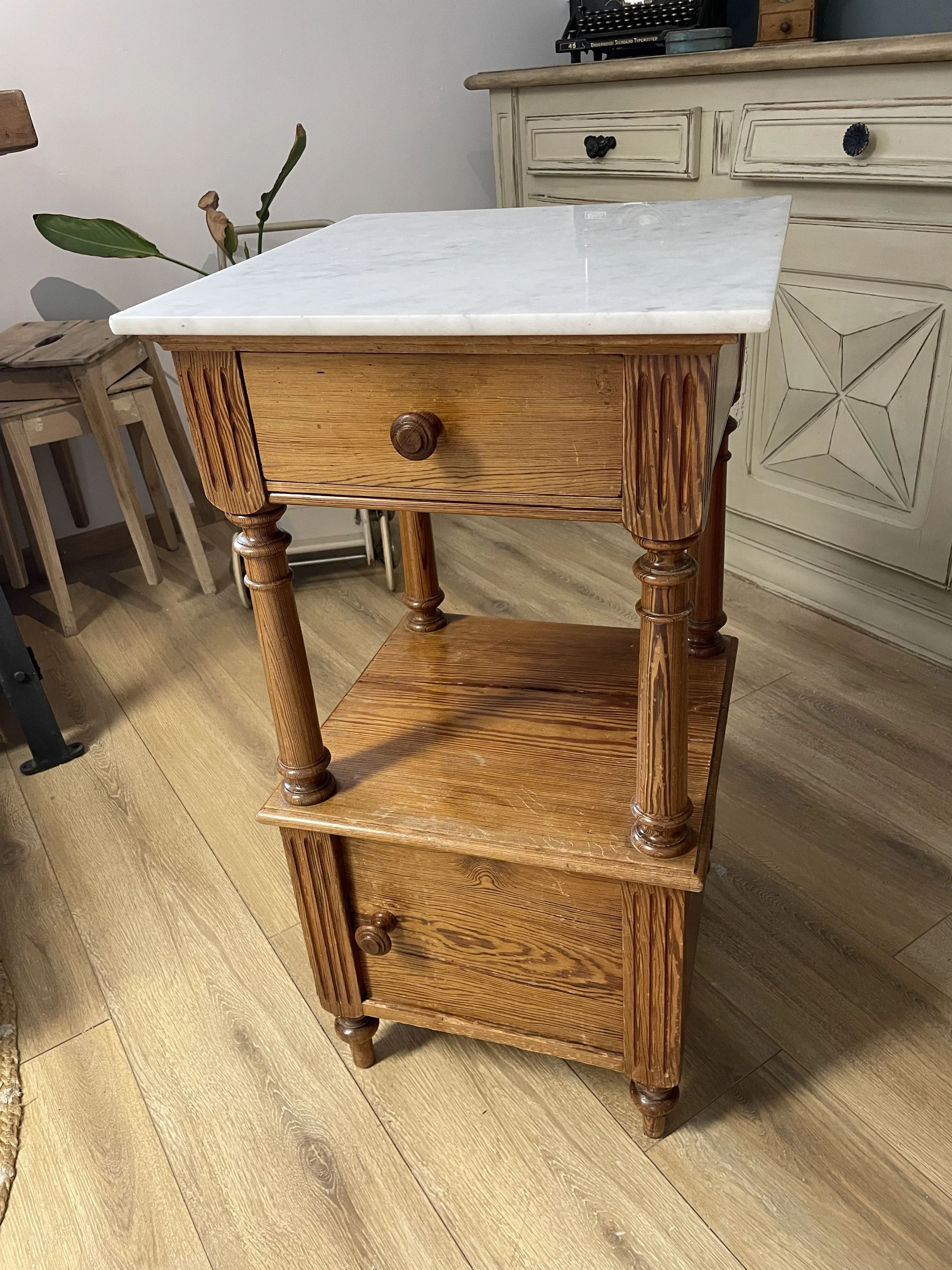 Petit meuble en bois avec deux tiroirs, dessus en marbre blanc, dans une pièce avec plancher en bois clair.