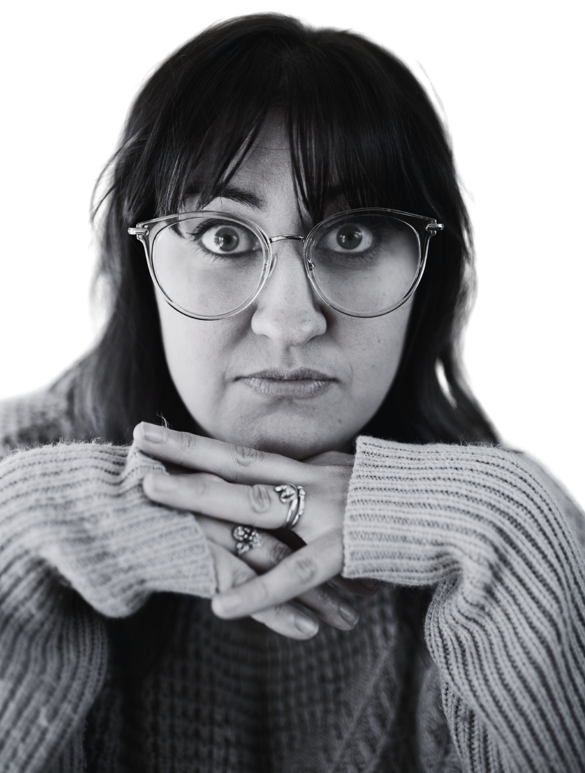 Black and white photo of a woman with glasses, resting her chin on her folded hands, wearing a striped sweater.