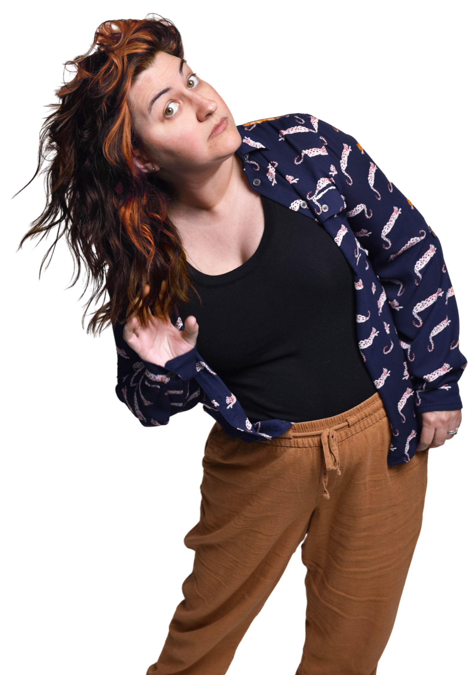 A woman with wavy, reddish-brown hair styled in loose curls, wearing a navy blue shirt with white and red pattern, a black top underneath, and tan pants, looking directly at the camera with a serious expression.
