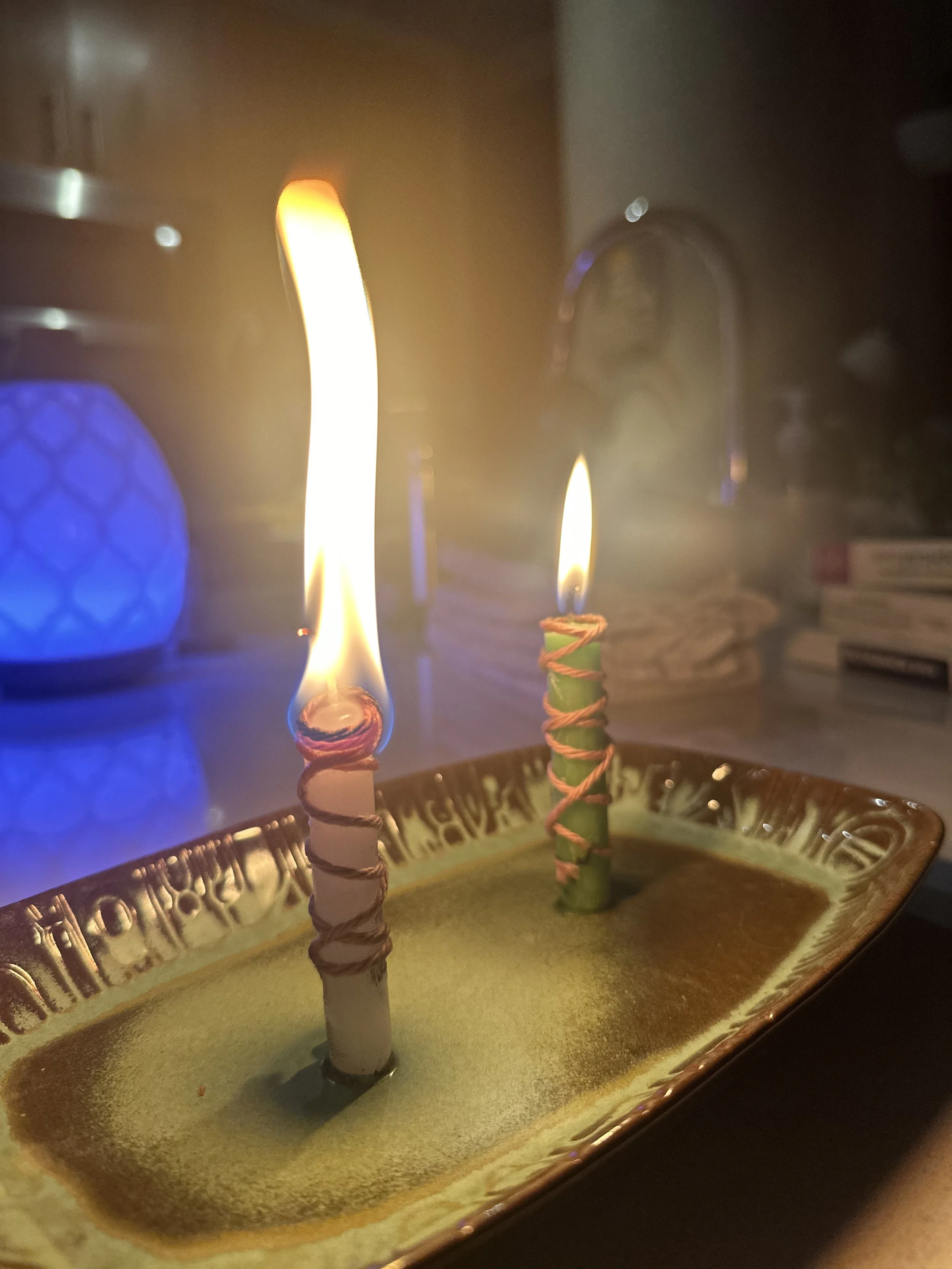 Two lit candles with spiral wraps in a ceramic dish, in a dimly lit kitchen.