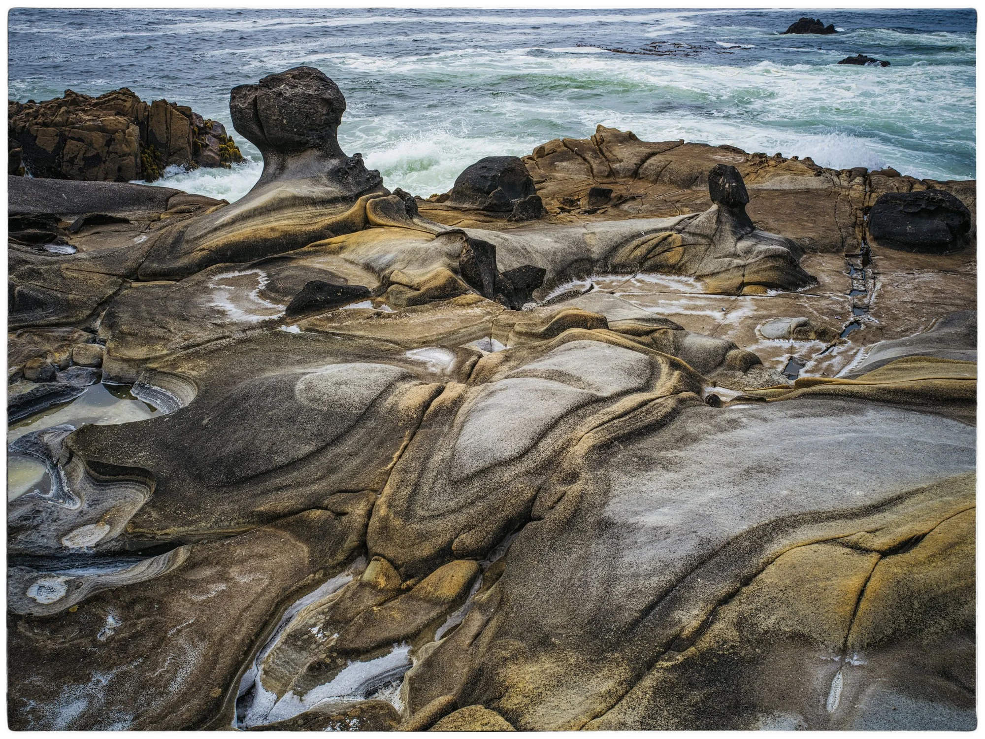 Rock formations on the shoreline with ocean waves crashing in the background