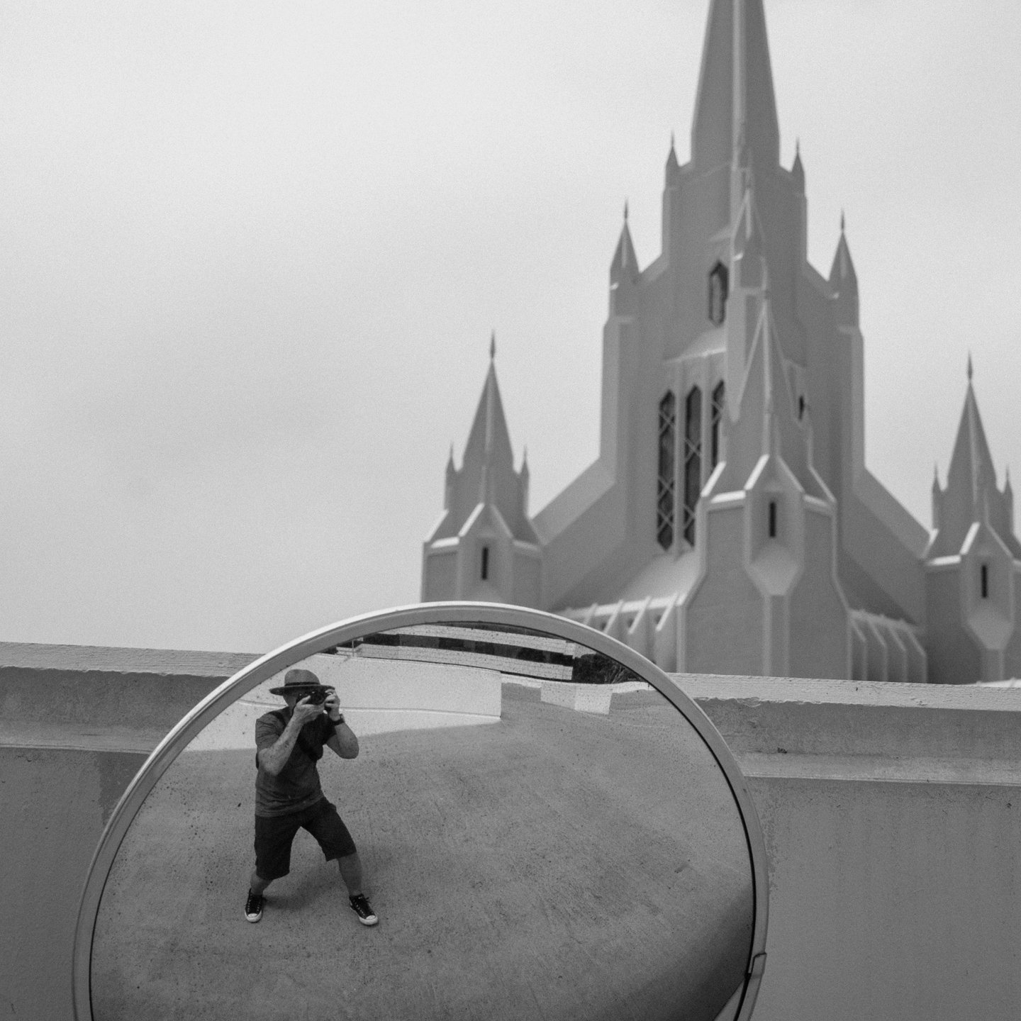 A person taking a photo of themselves reflected in a round mirror, with a large church or cathedral in the background.