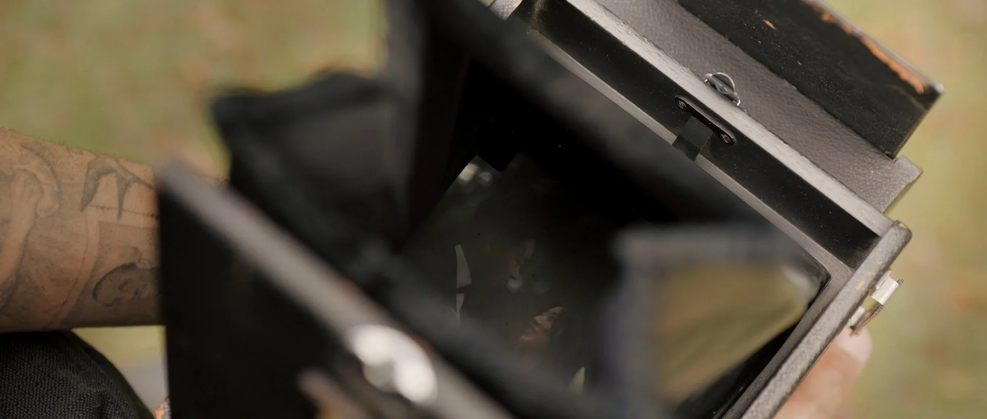 Close-up of an old medium format camera with a dark interior viewfinder, showing a bride and groom reflected inside the viewfinder.