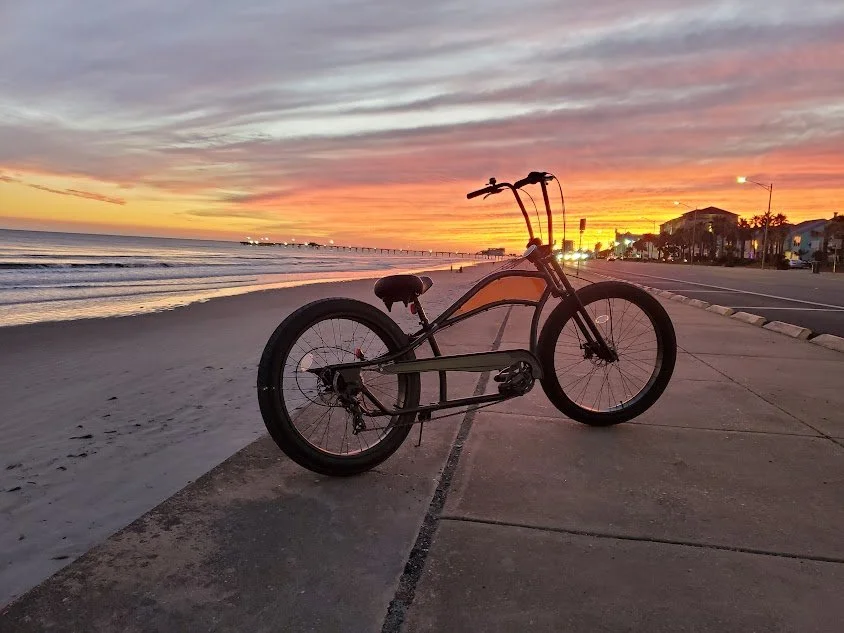 A bike parked on a sidewalk near the beach during a colorful sunset.
