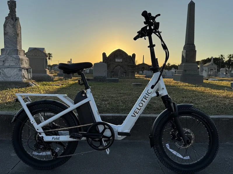 Electric bicycle parked in a cemetery during sunset, with tombstones and monuments in the background.