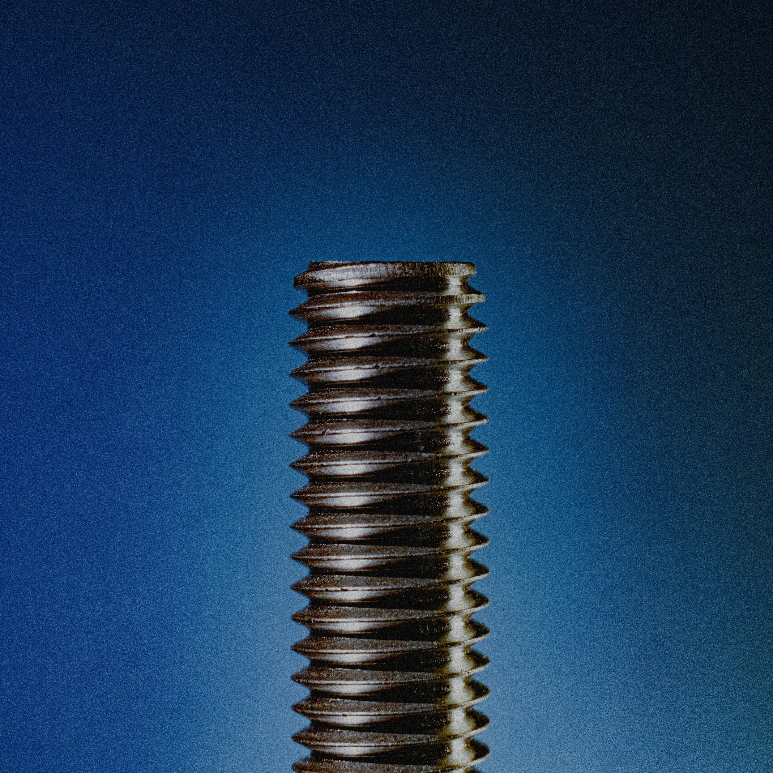 Close-up of a metallic screw with a flat, slotted head, placed against a dark blue background.