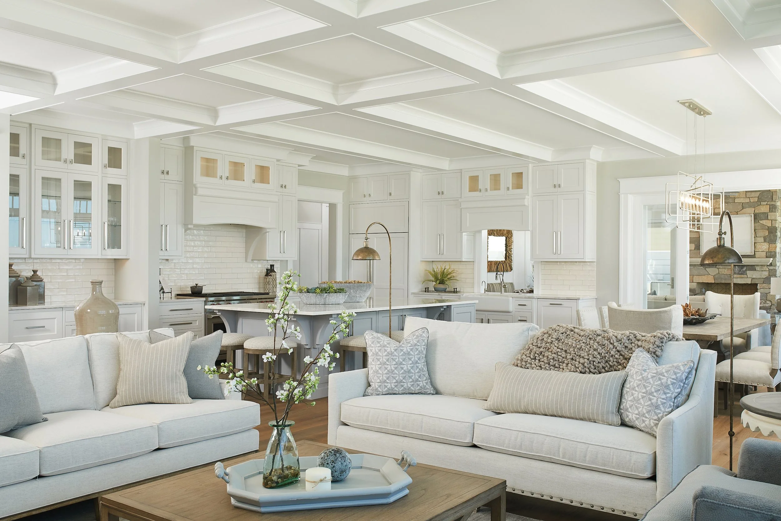Bright open-concept living room and kitchen with white cabinetry, stone accents, and neutral furniture.