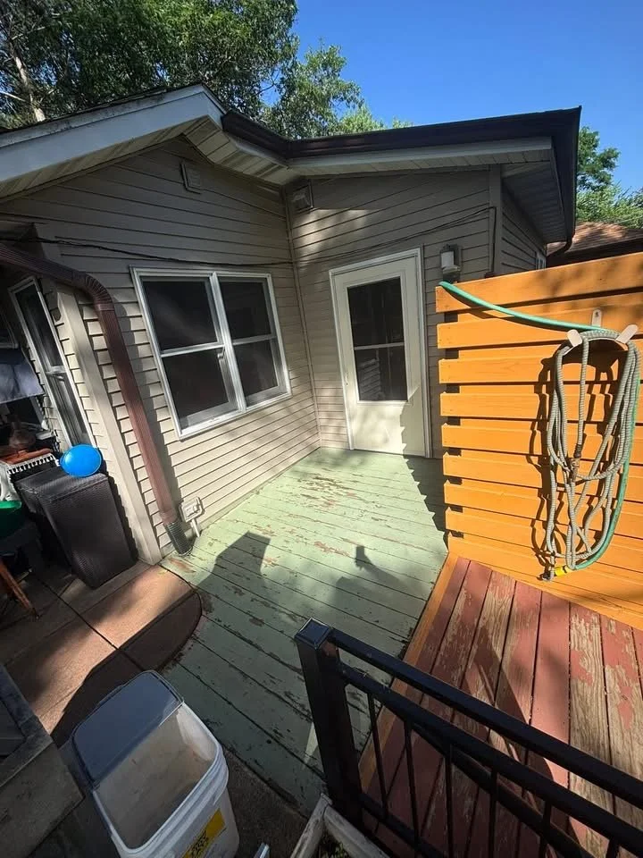 Back patio with sliding glass door, window, wooden deck, some outdoor furniture, and a wooden privacy screen with a hose hanging on it.
