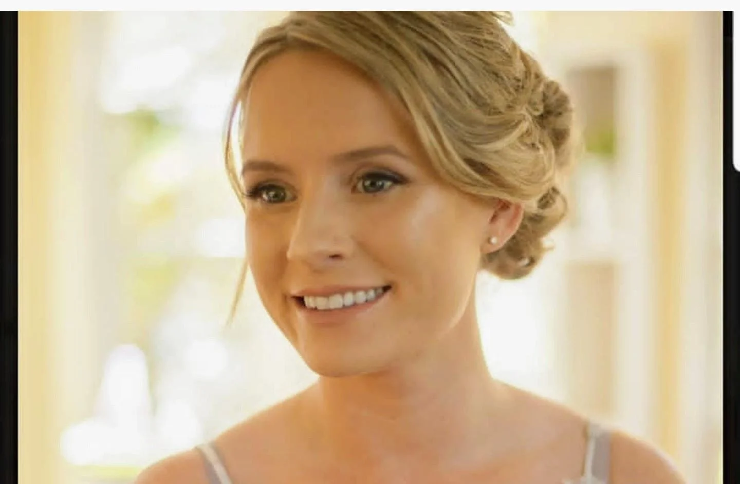 A woman with styled blond hair, earrings, and a bright smile.