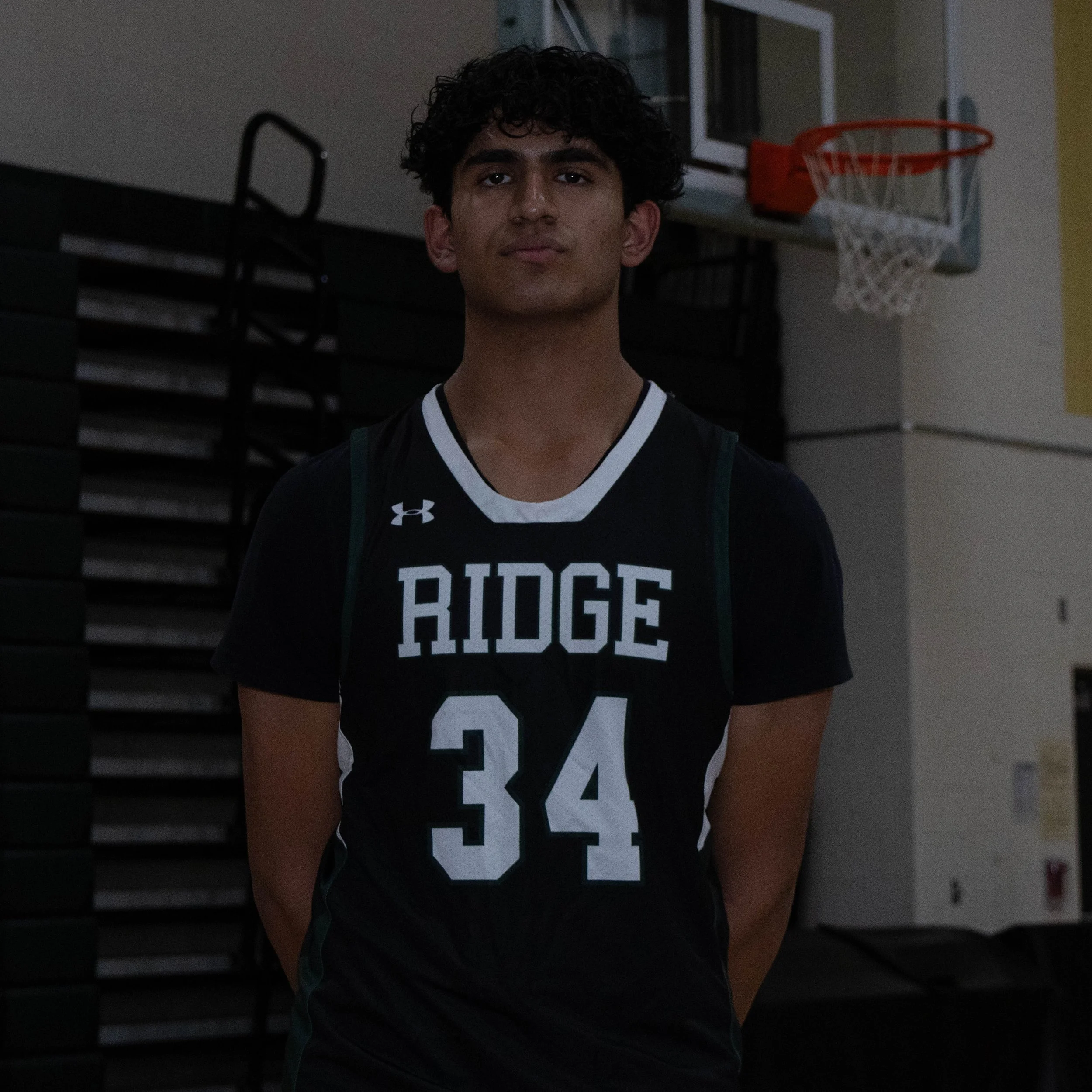 A young basketball player standing in a gymnasium, wearing a black jersey with the word 'RIDGE' and the number 34.