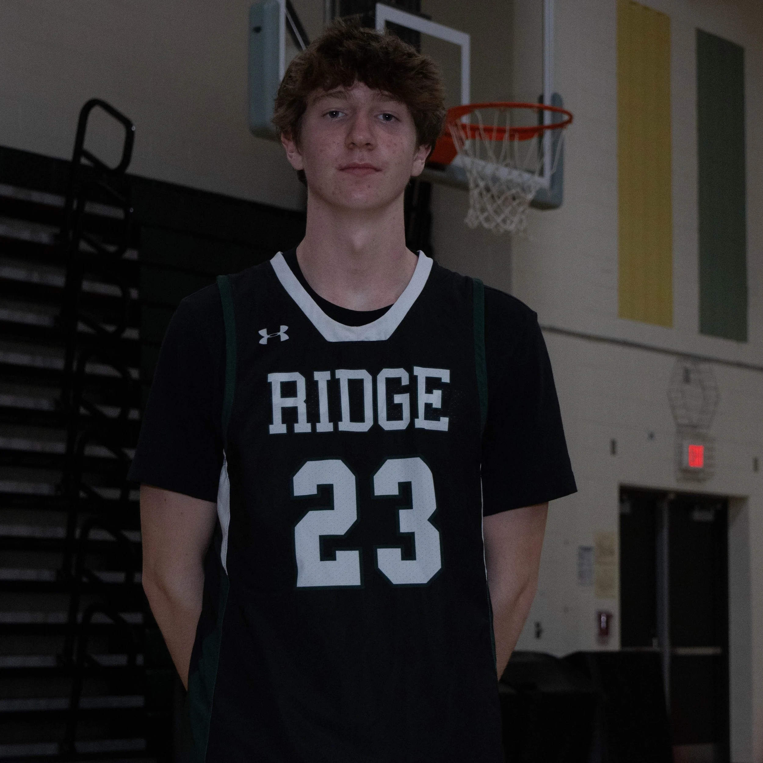 A young male basketball player in a black Ridge jersey with number 23 standing in a gymnasium.