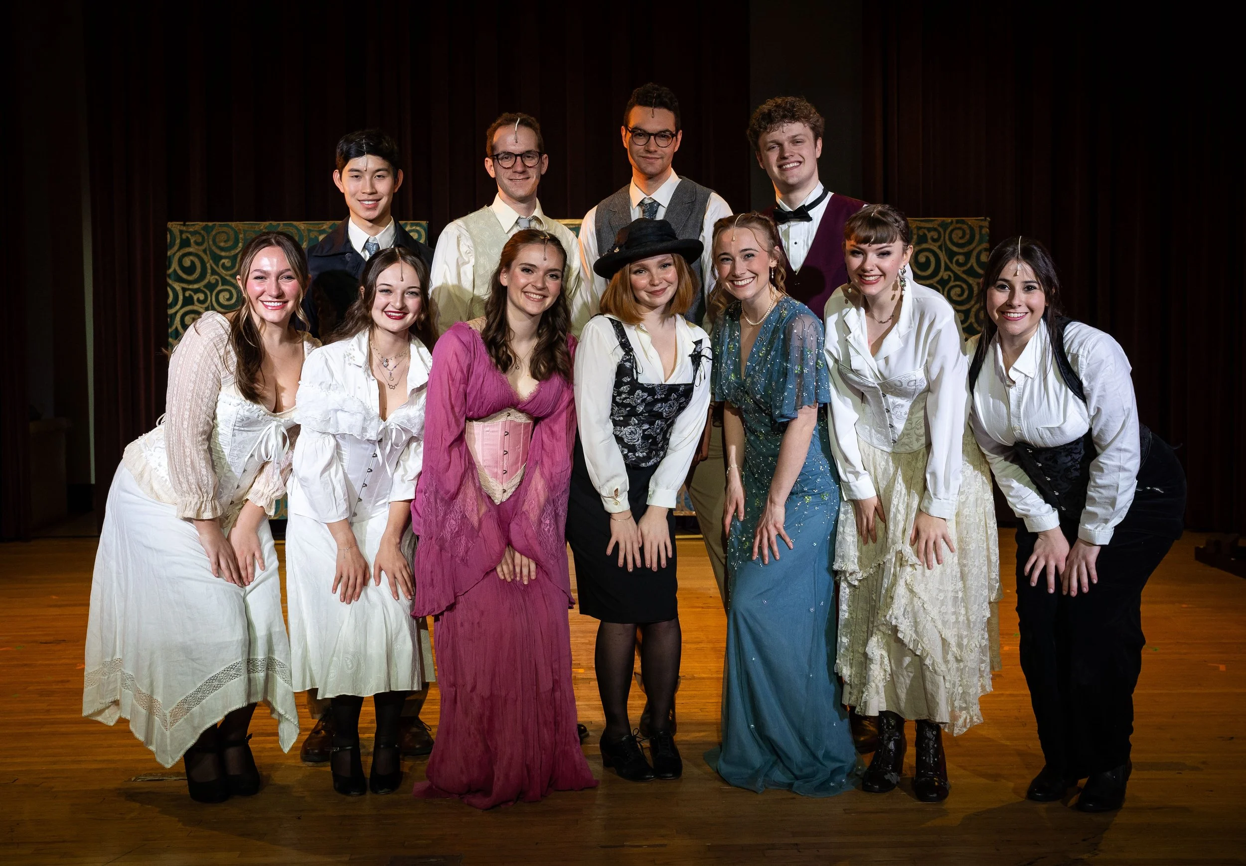 Group of young actors in costumes on stage, smiling after a play or performance.