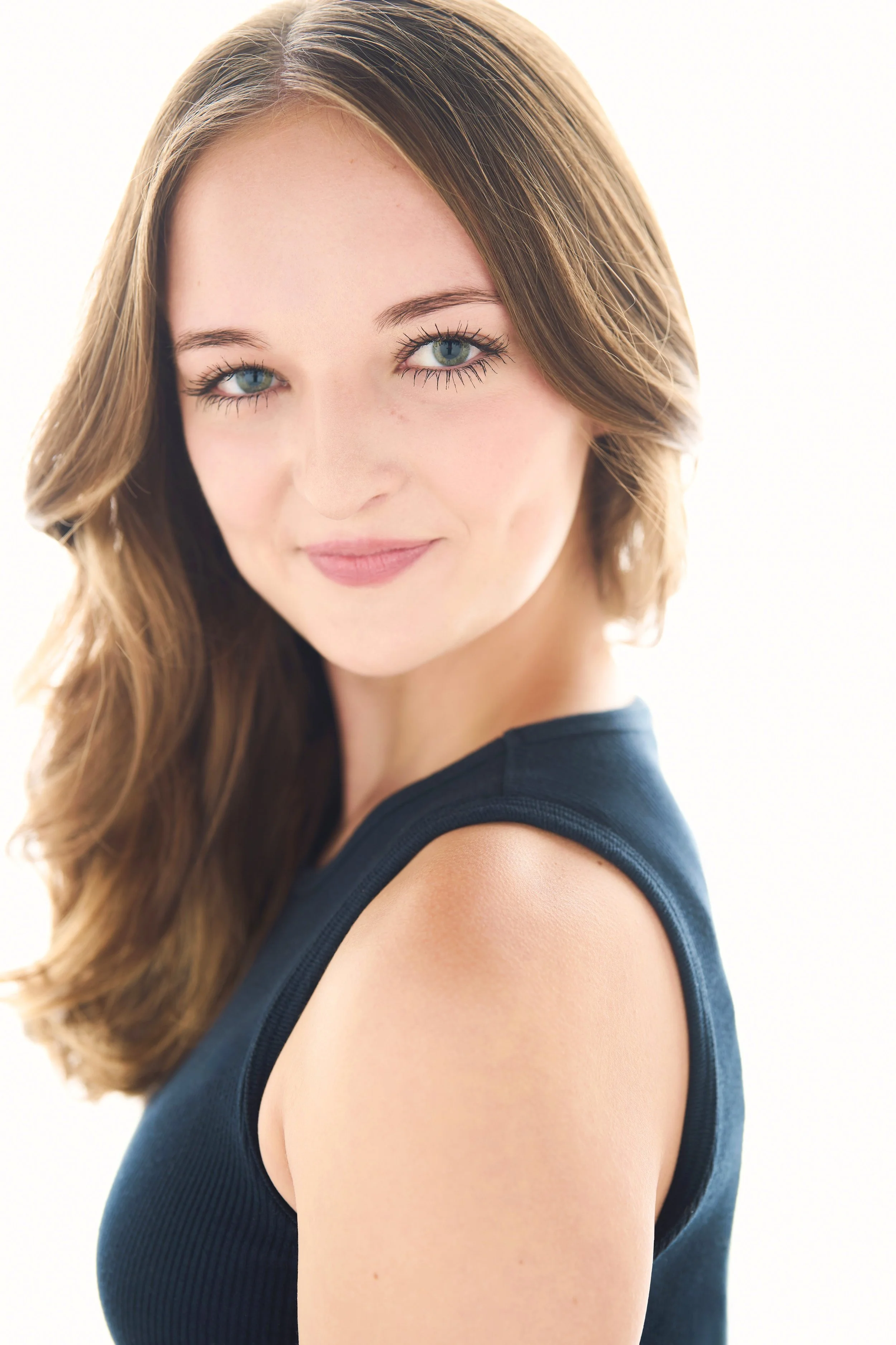 Sarah Novak with long brown hair and blue eyes, wearing a sleeveless black top, smiling softly at the camera with a white background.