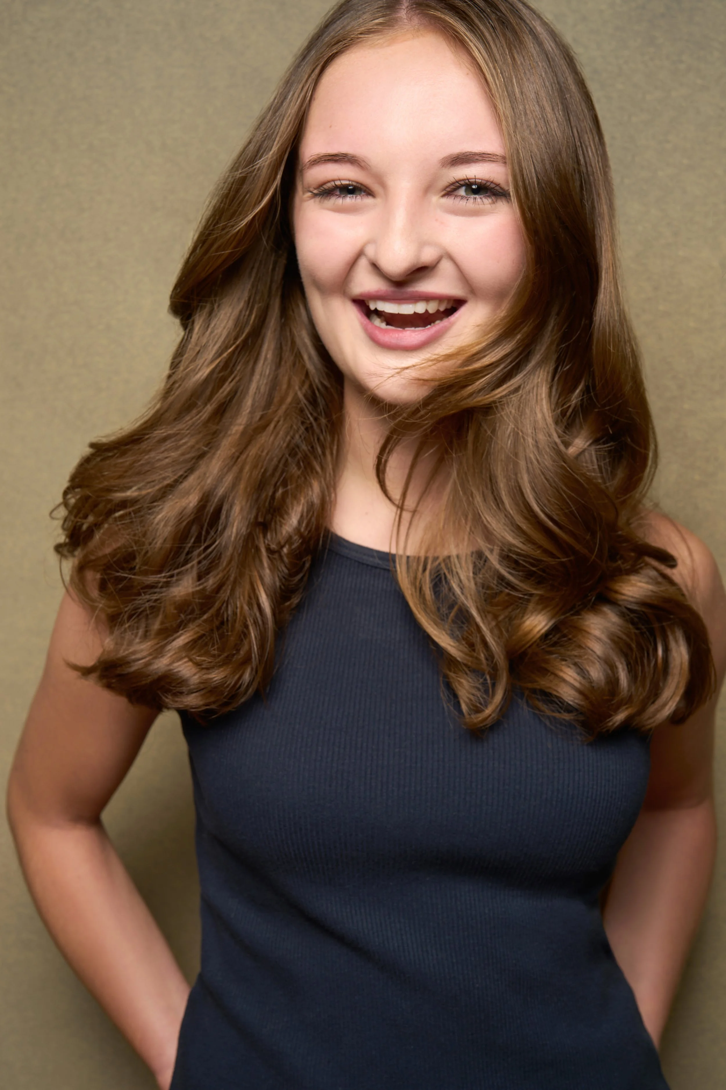 Sarah Novak with long, wavy auburn hair smiling and looking at the camera, wearing a navy sleeveless top, with a beige background.