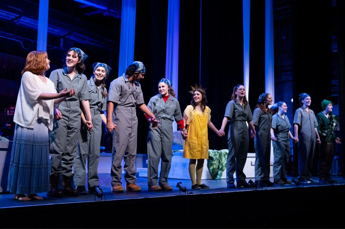 The cast of a theatrical play taking a bow on stage, with actors dressed in costumes and holding hands in a line.