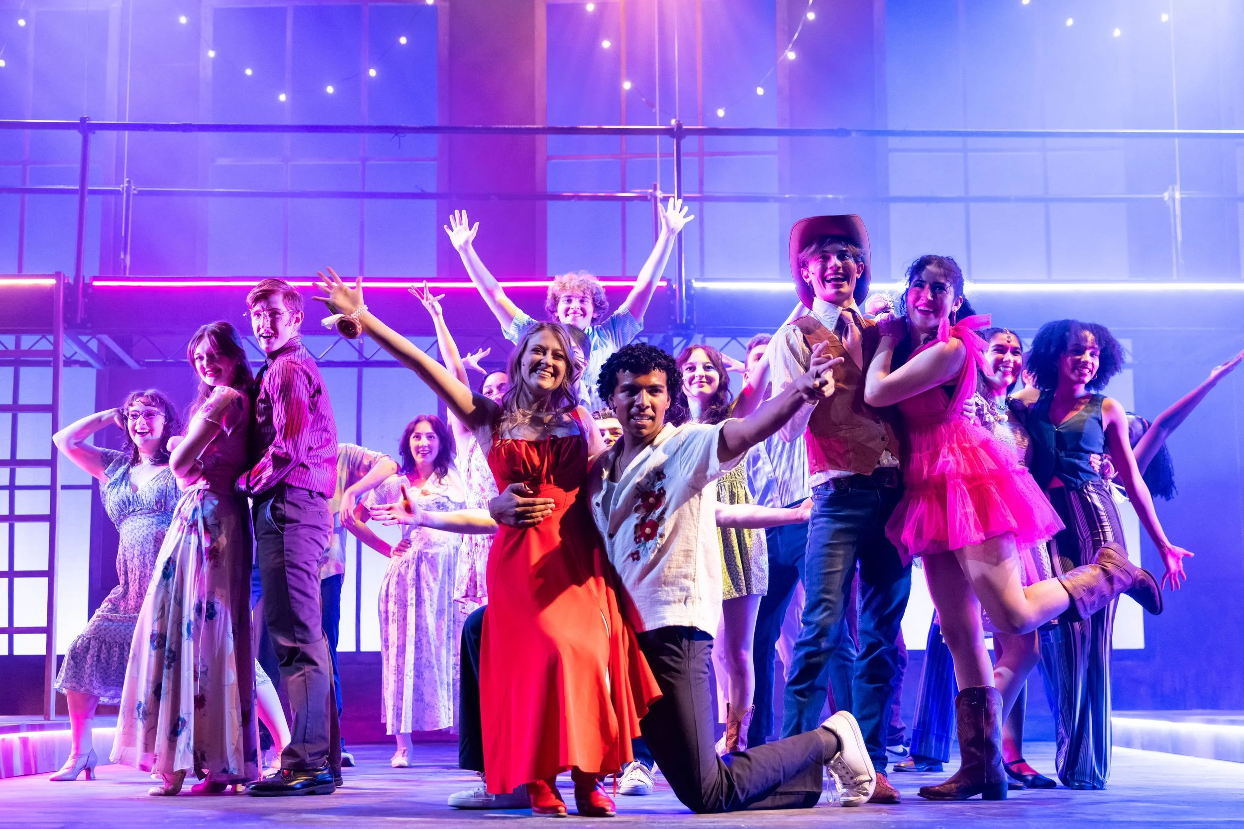 Footloose at Northwestern University with a diverse group of actors in colorful costumes, smiling and striking various poses, under vibrant stage lighting.