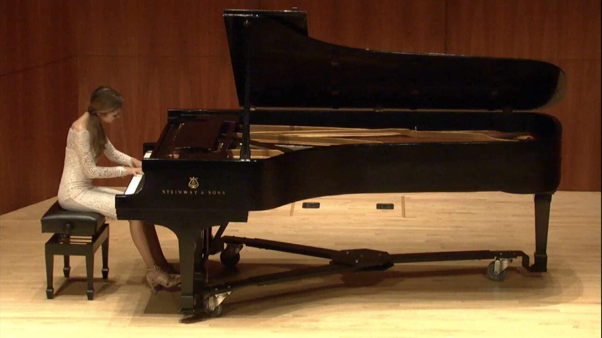 Sarah Novak playing piano. Woman in a white dress playing a grand piano on stage.