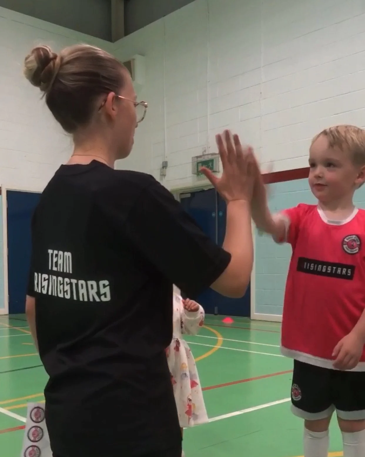A woman and a young boy in sports uniforms giving each other a high five in a gymnasium.