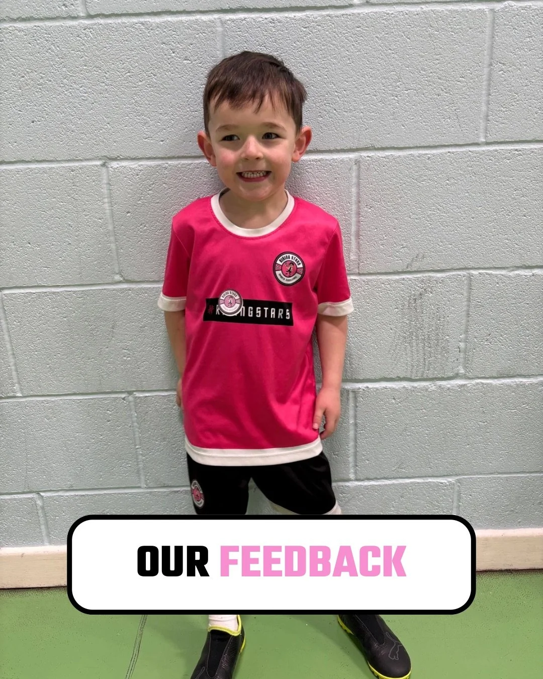 Young boy smiling, standing against a light gray cinder block wall, wearing a pink and white sports jersey with black shorts, black sports shoes, and holding his hands behind his back. Text overlay reads 'Our Feedback'.