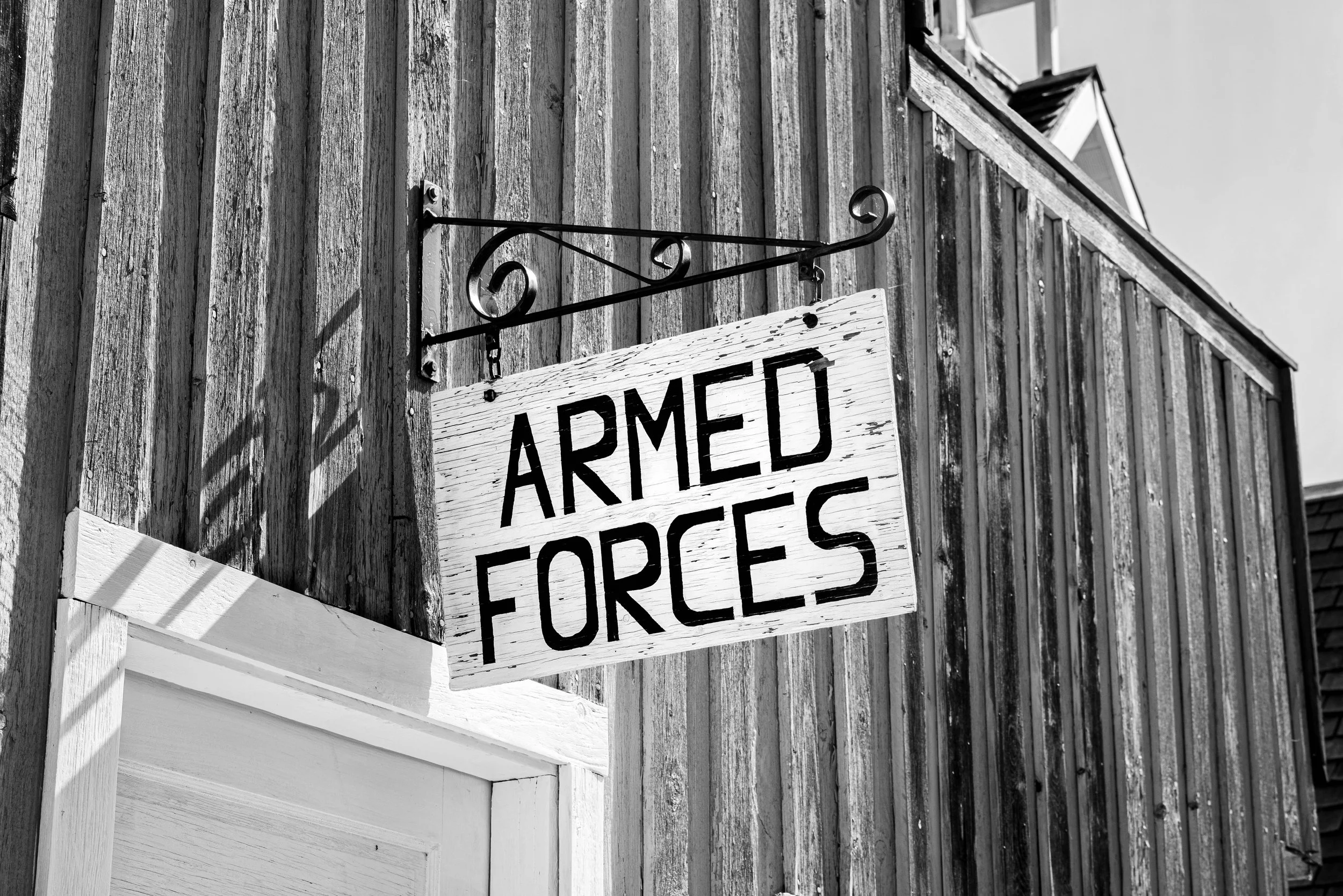 Wooden building exterior with a sign that reads "Armed Forces" hanging from a metal bracket.