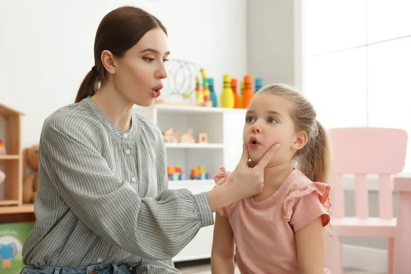 A woman is examining a young girl's throat in a room filled with toys and colorful objects.
