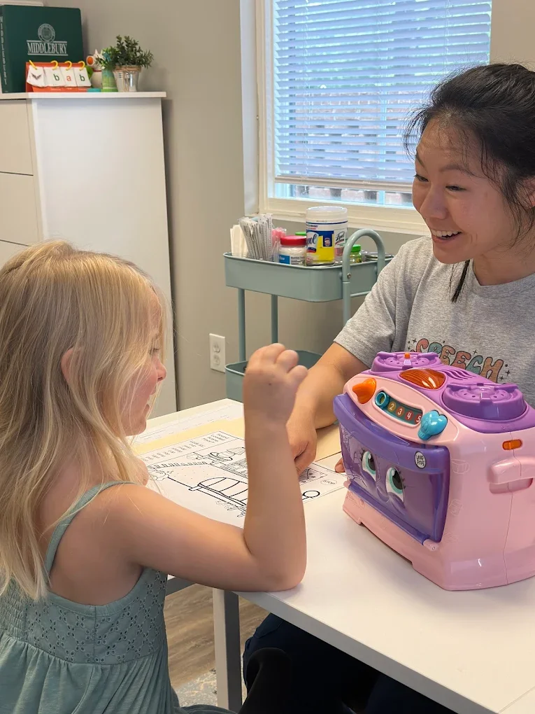 A young girl and a woman are sitting at a table playing arm wrestling with a toy cash register, smiling and enjoying their time together.