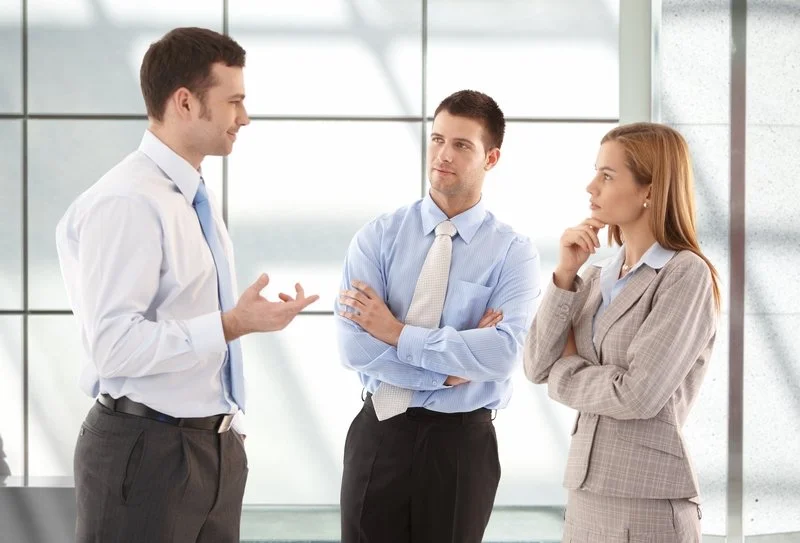 Three business professionals engaged in a discussion in a modern office setting.
