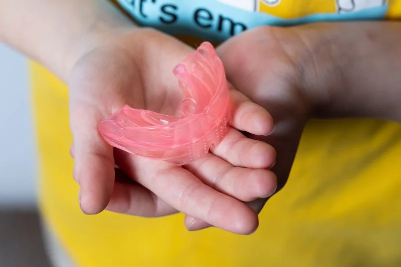 A person holding a pink mouth guard in their hand.