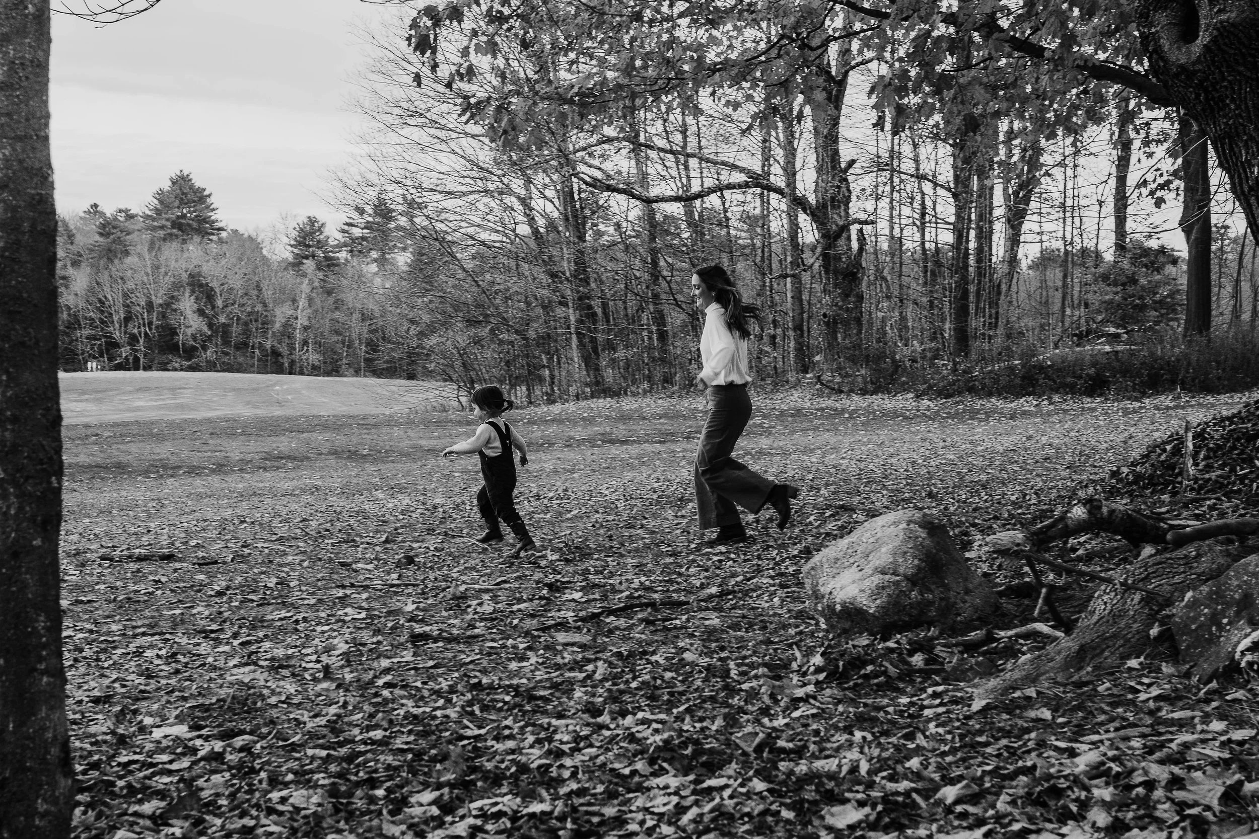 Mother and daughter running and playing together during a fall mini photo session with autumn foliage in the background.