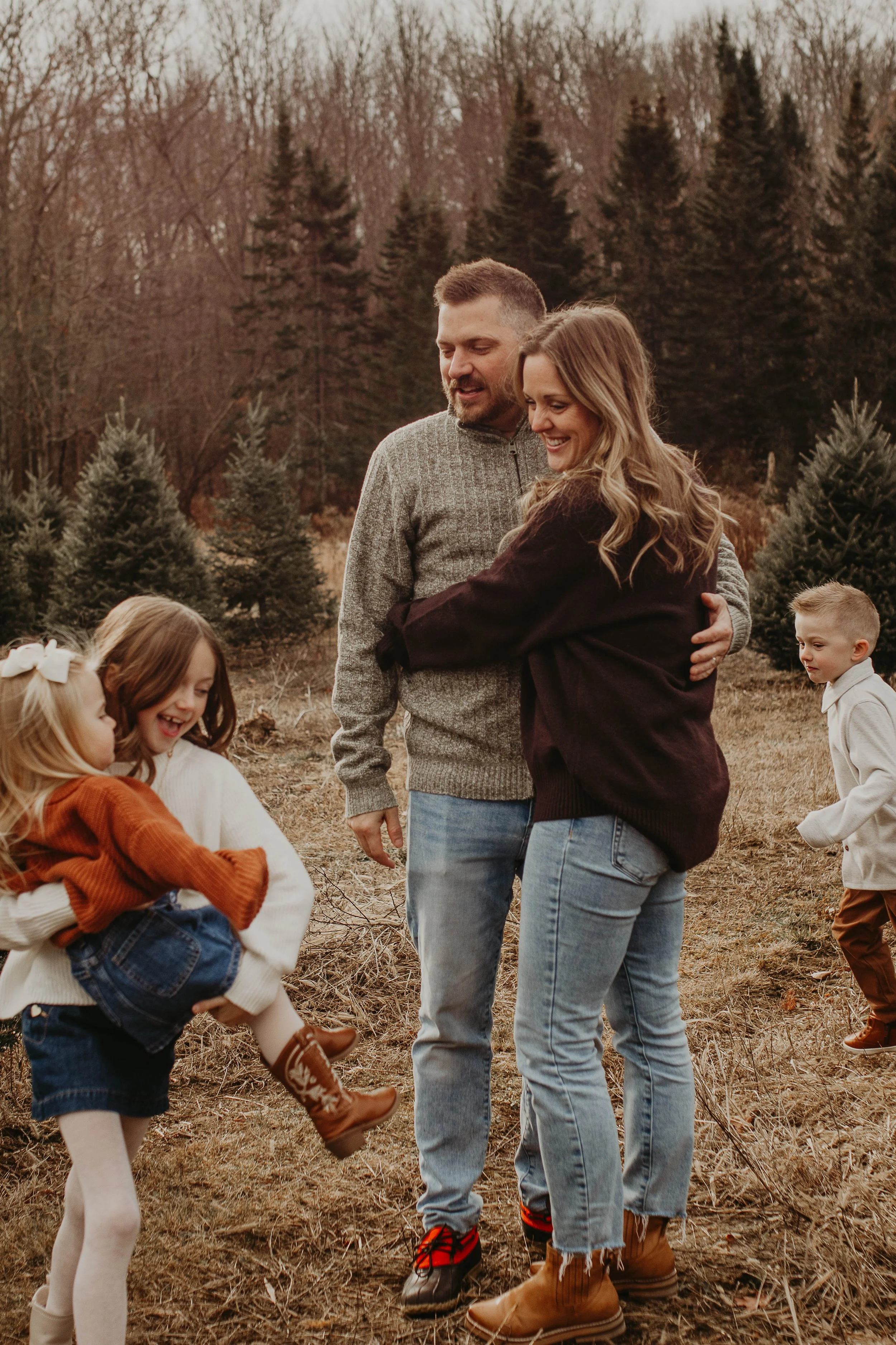 A family of five, including two adults and three children, enjoying a day outdoors in a wooded area with pine trees, during the fall.