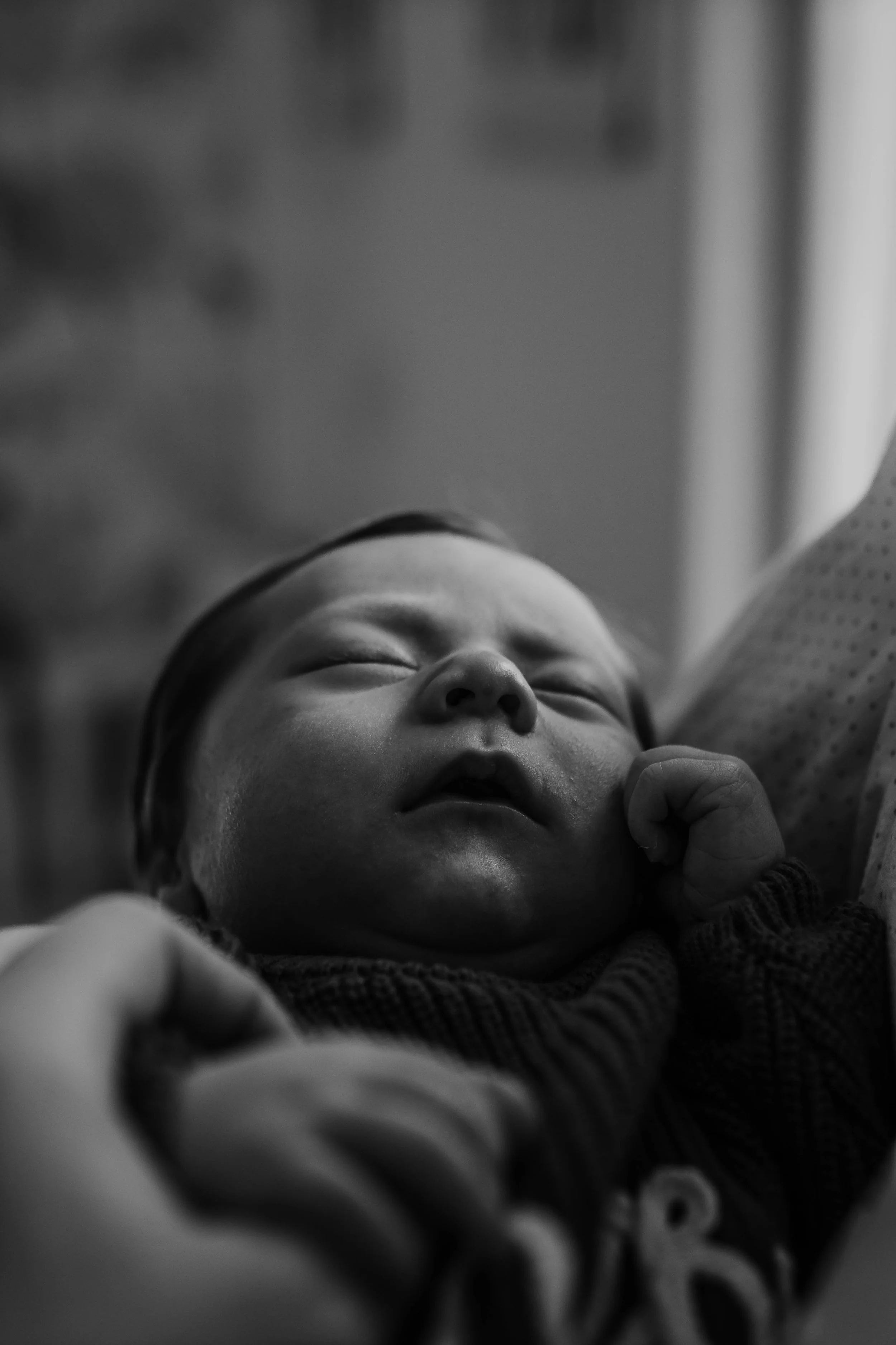 Black and white photo of a newborn baby sleeping, cradled in someone's arms.
