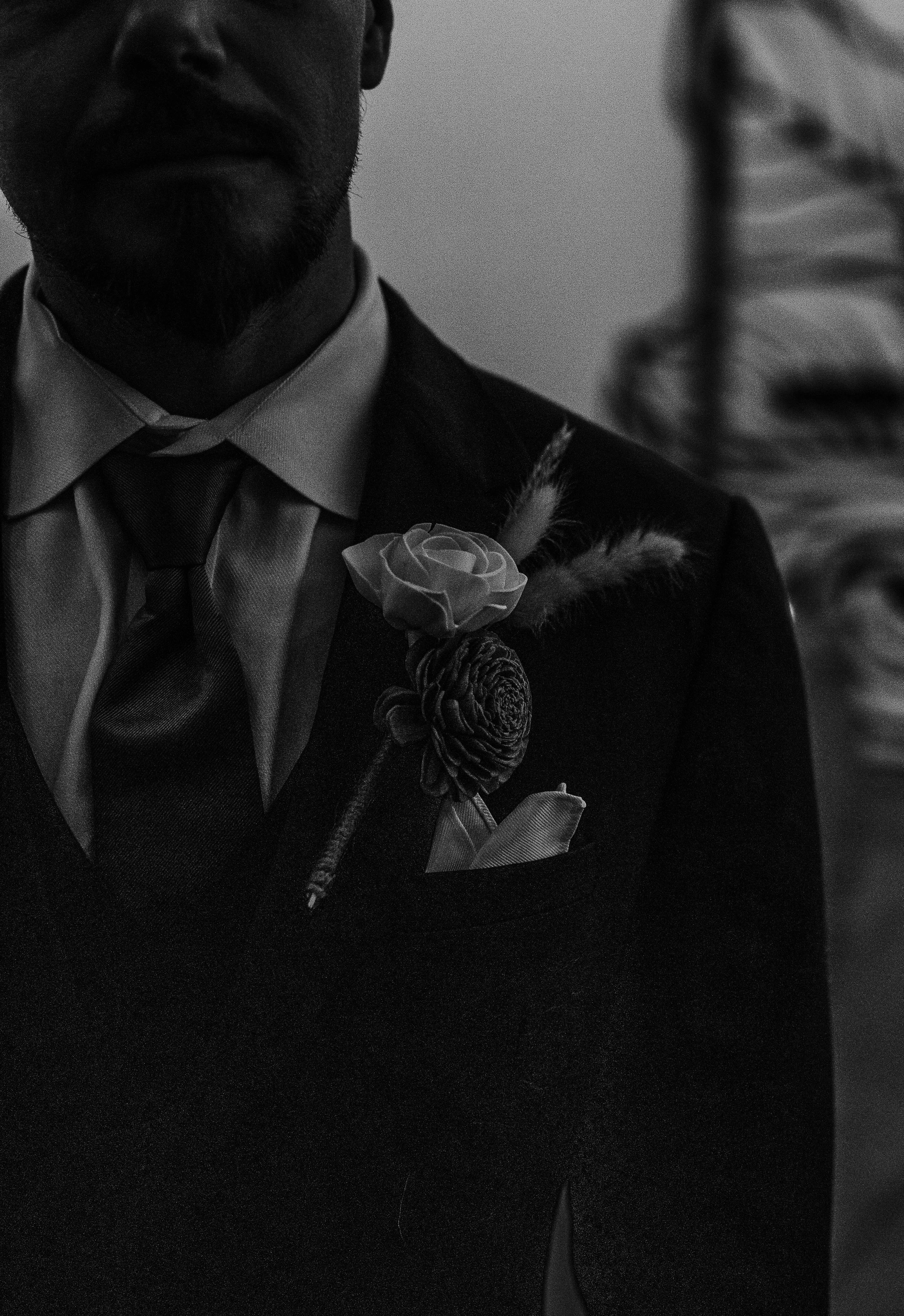 Close-up of a man dressed in formal attire, wearing a suit, tie, and boutonniere, in black and white.