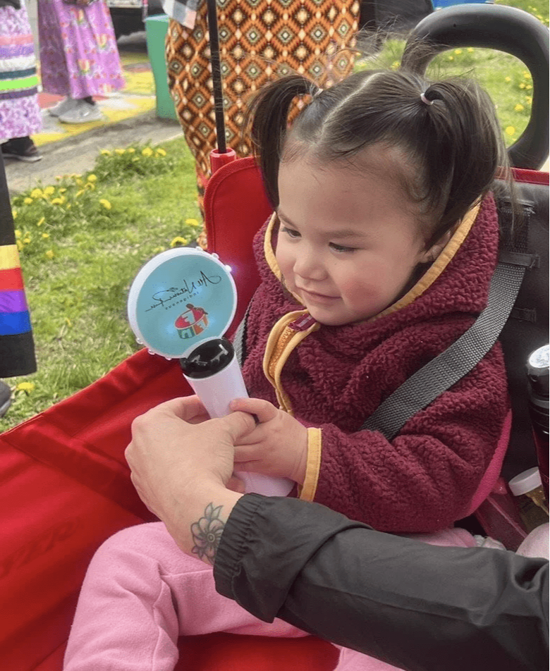 Young child in a stroller holding a colorful toy at an outdoor cultural event