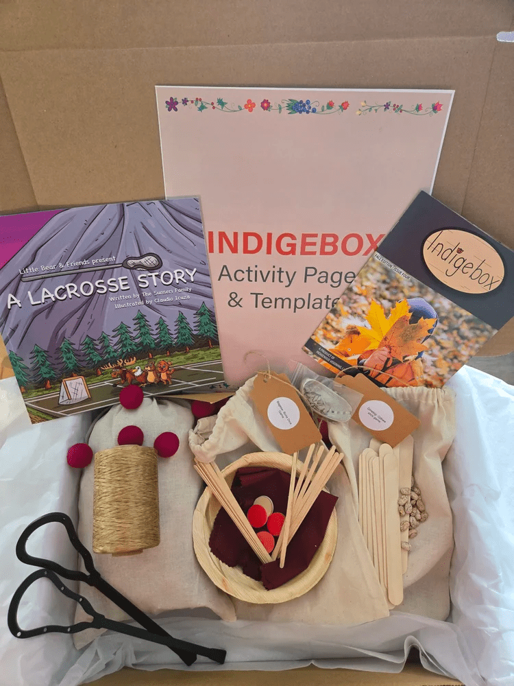 Indigebox activity kit with a lacrosse storybook, activity templates, craft supplies, wooden sticks, felt pieces, yarn, and red pom-poms