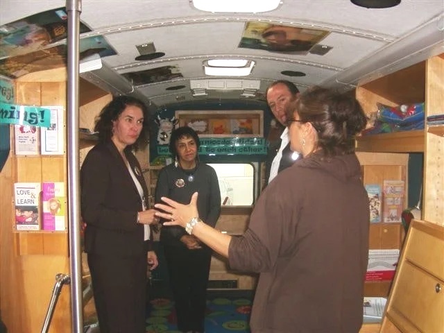 Four adults conversing inside a colorful mobile library or educational bus.