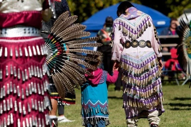 Native American dancers in colorful traditional regalia and feathered headdresses at an outdoor powwow
