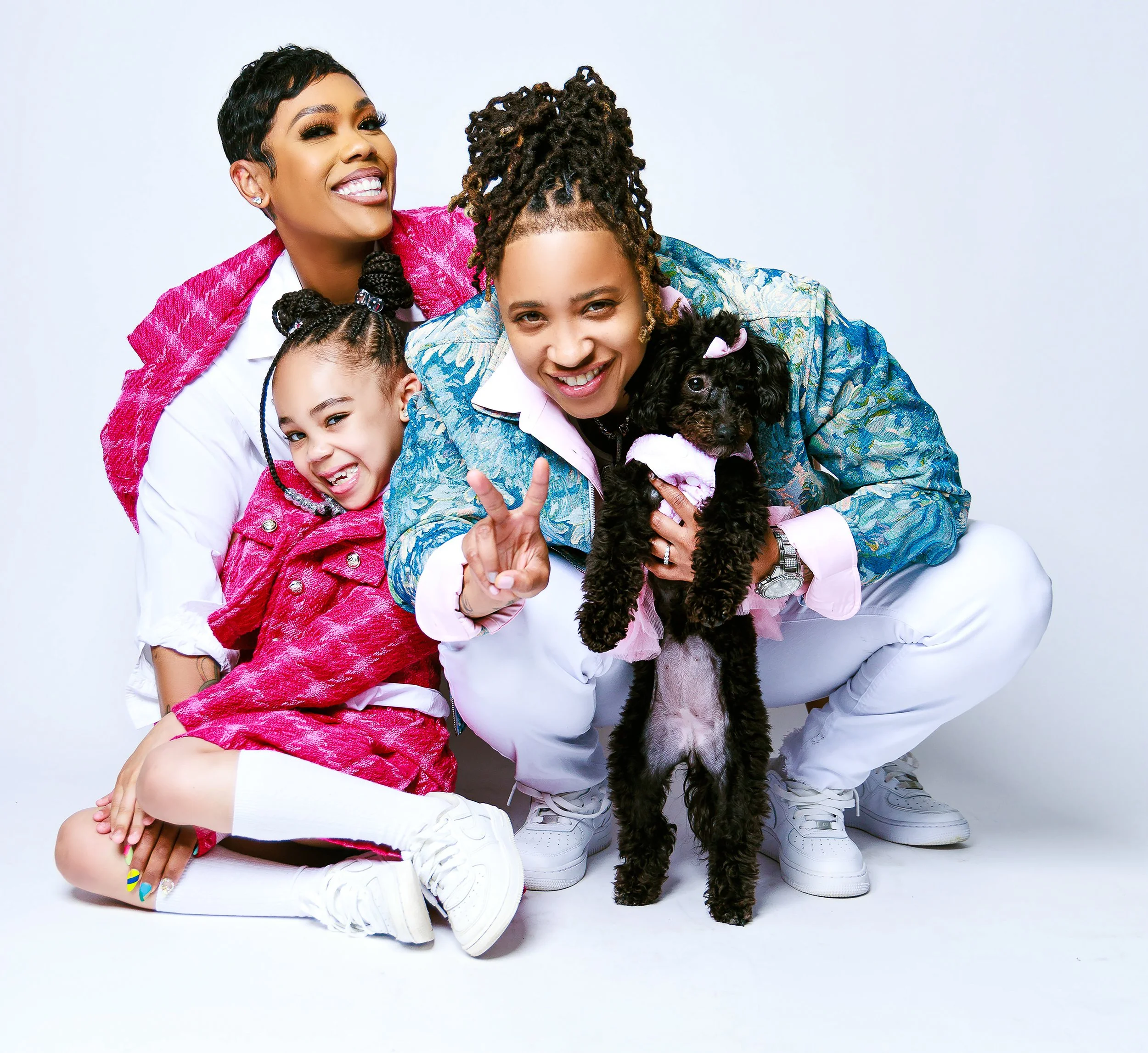 Three women and a puppy posing together, with two women making a peace sign and all smiling.