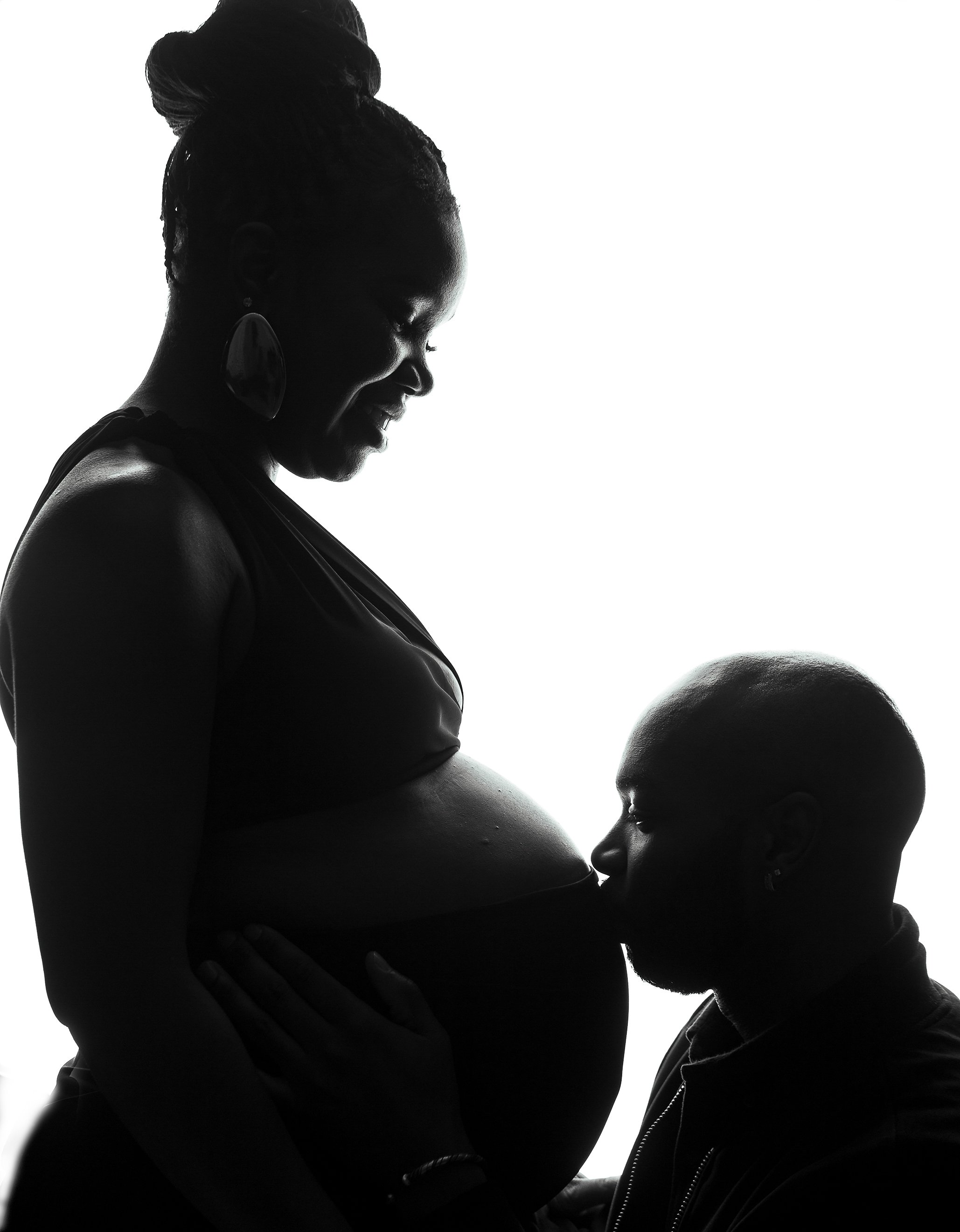 Silhouette of a pregnant woman and a man, with the man kissing the woman's pregnant belly.