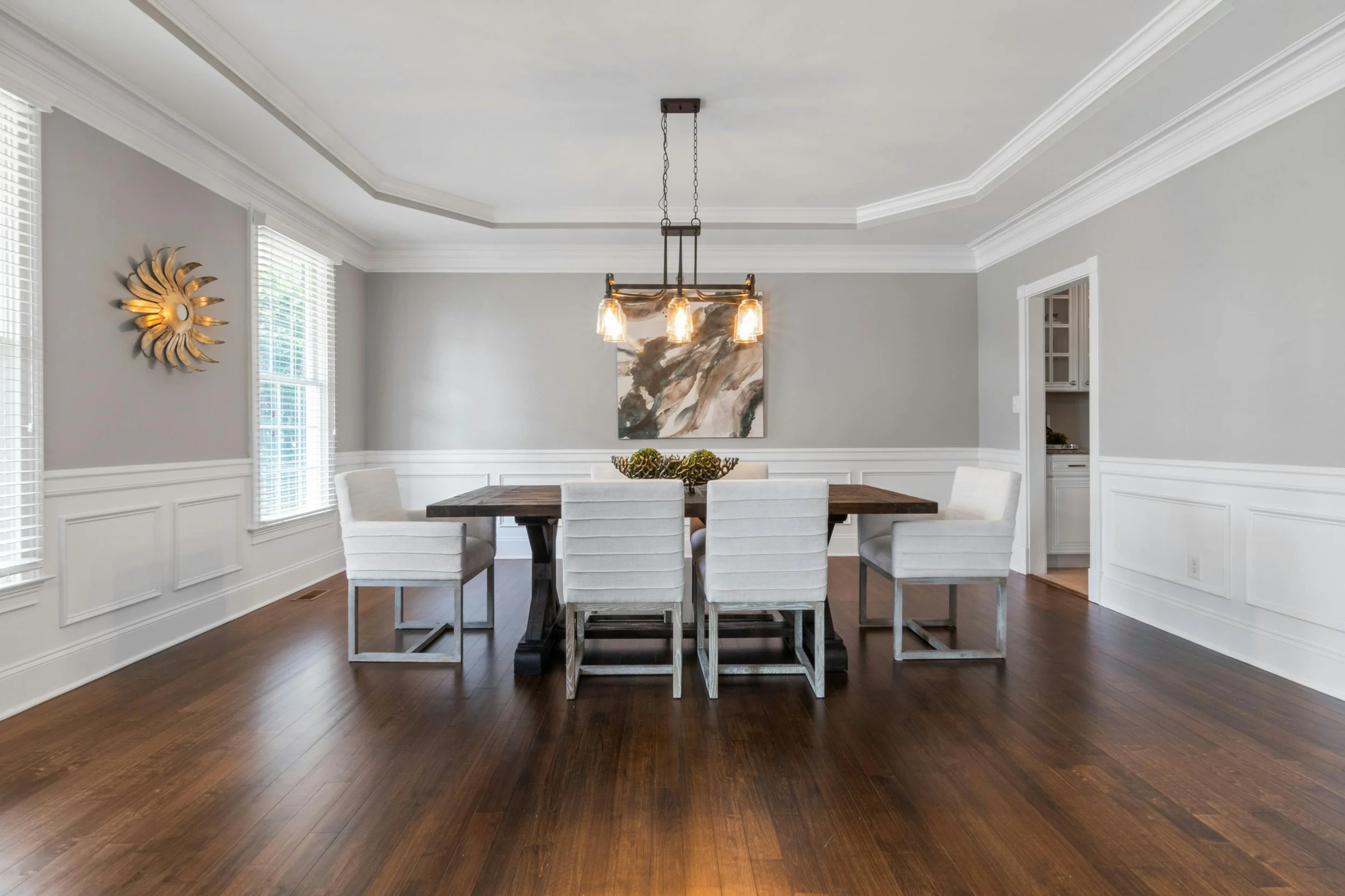 modern dining room with dark hardwood flooring, white and grey walls, and a large dining table in the centre.