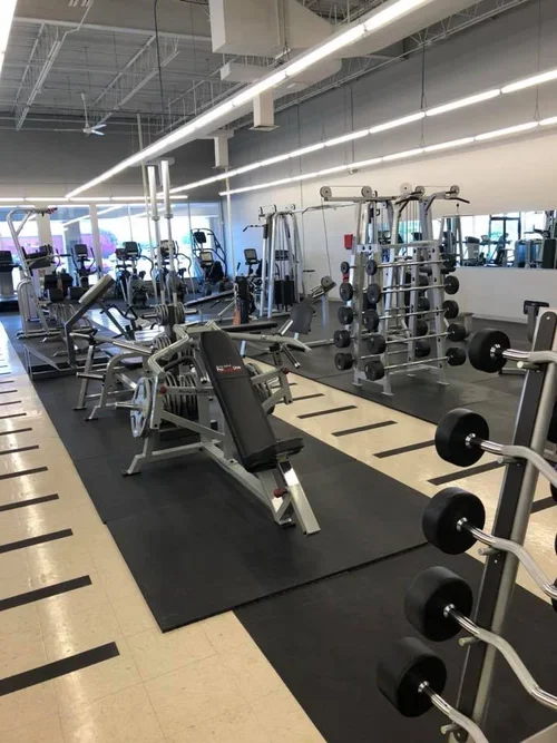 Indoor gym with weightlifting equipment including barbells, dumbbells, and weight machines.