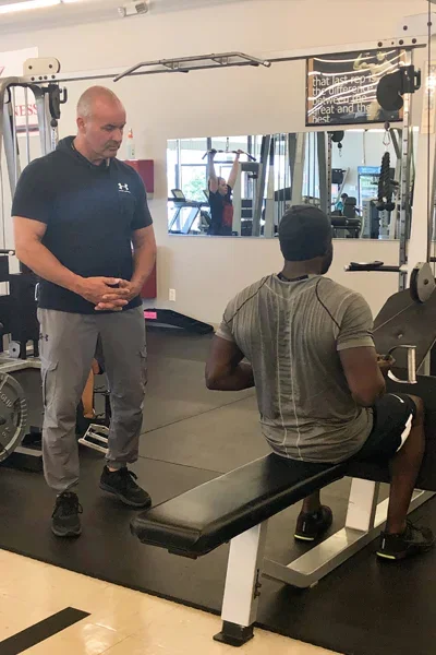 Personal trainer coaching a man doing seated leg press at a gym.