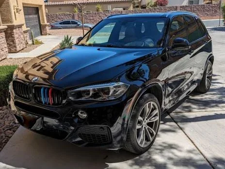 Black BMW SUV parked in driveway with houses and sidewalk in background