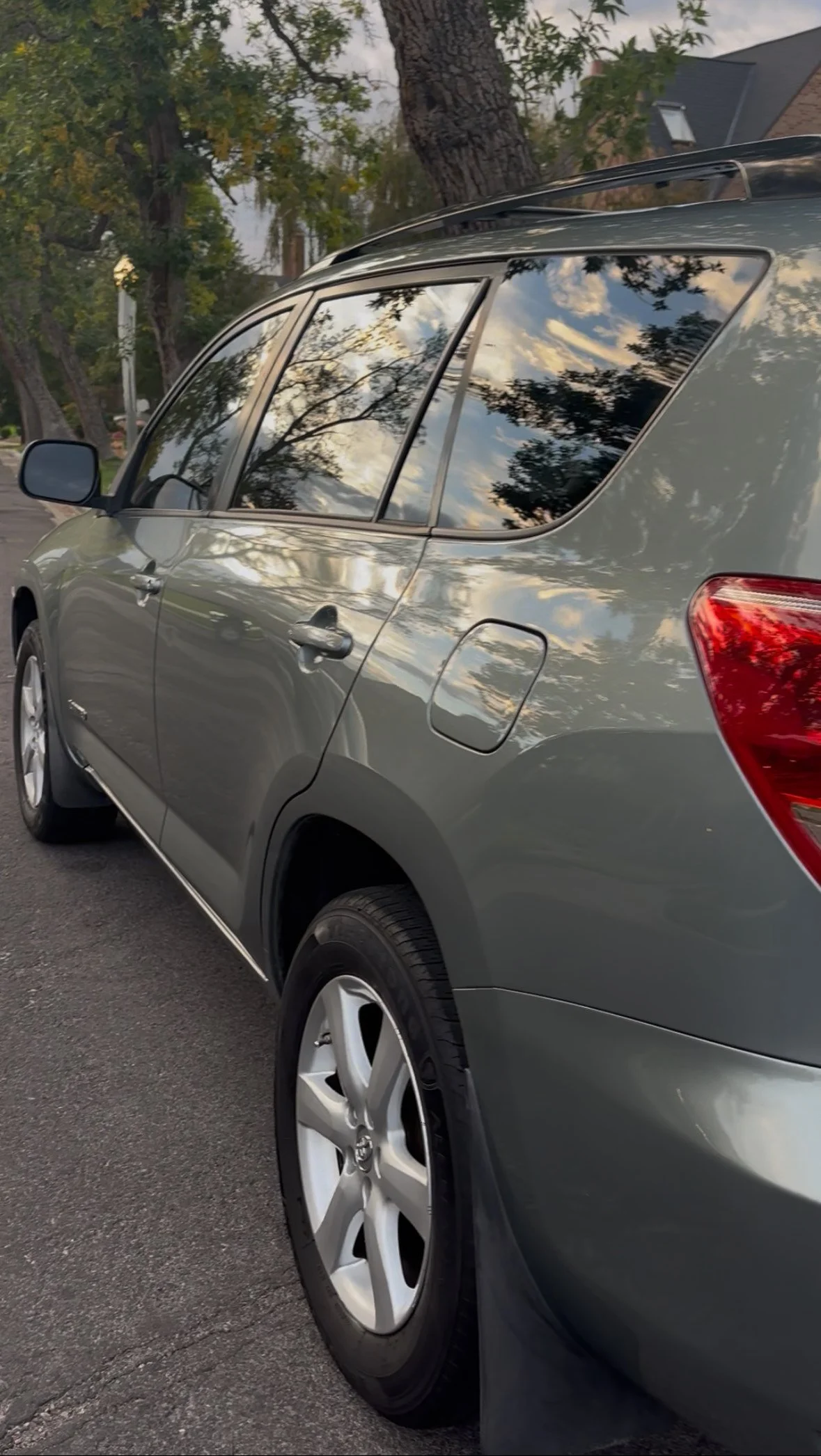 Side view of a gray SUV parked on the street, with reflections of trees and sky on the windows.