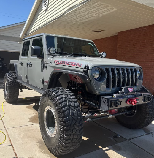 Gray Jeep Rubicon off-road vehicle with large tires parked in driveway near garage and house