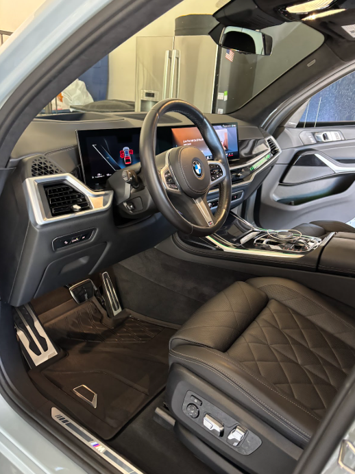 Interior of a modern BMW vehicle, showcasing the steering wheel, digital dashboard, center console, and black leather seat with diamond stitching.