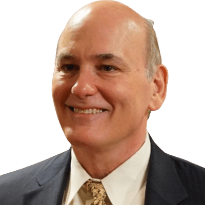 A smiling middle-aged man with short, light-colored hair, wearing a dark suit, white shirt, and patterned tie.