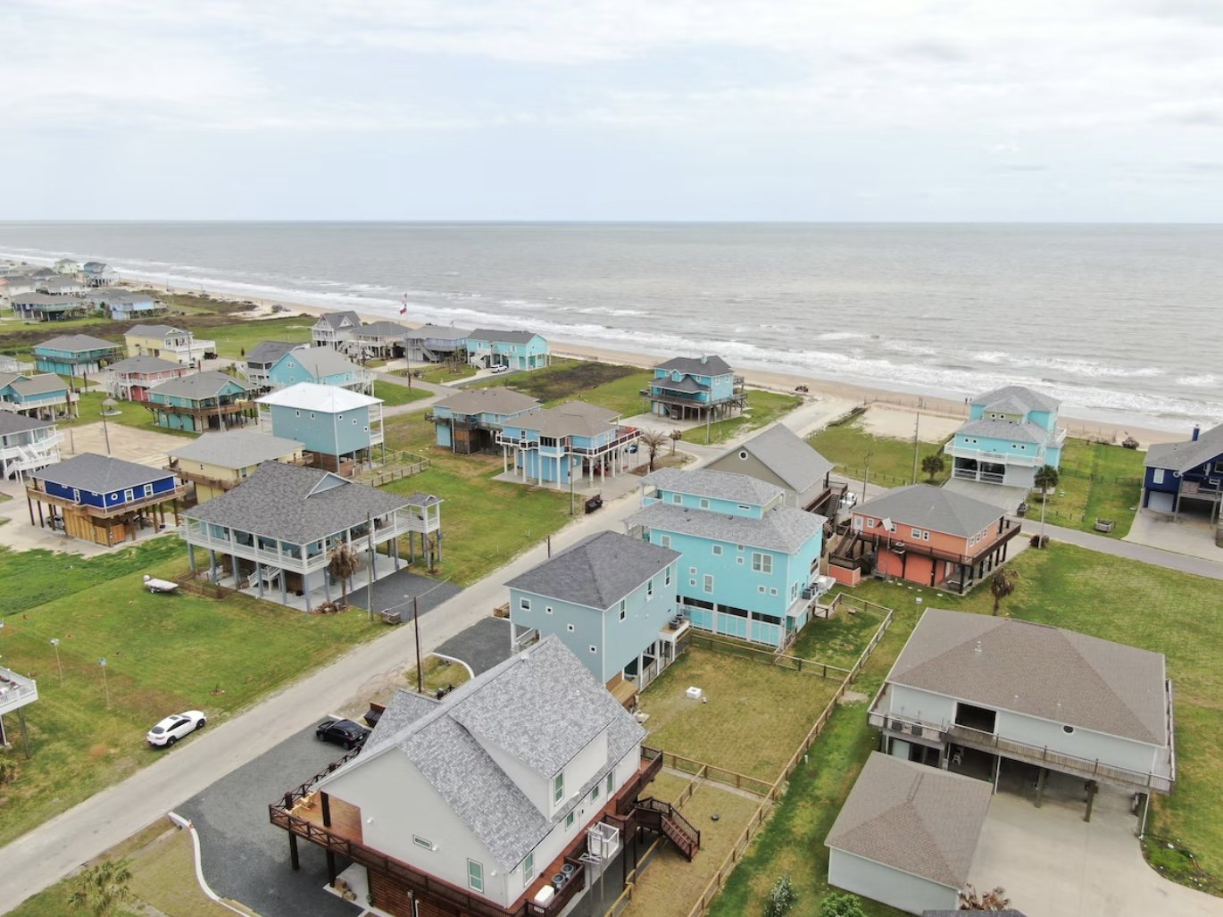 Aerial view of a beachfront neighborhood with colorful houses on stilts and access to the ocean.