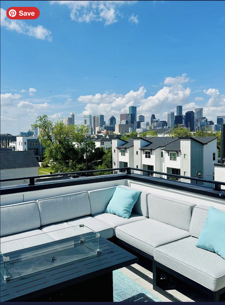 Skyline view of downtown city buildings from a rooftop with outdoor seating and a glass table.