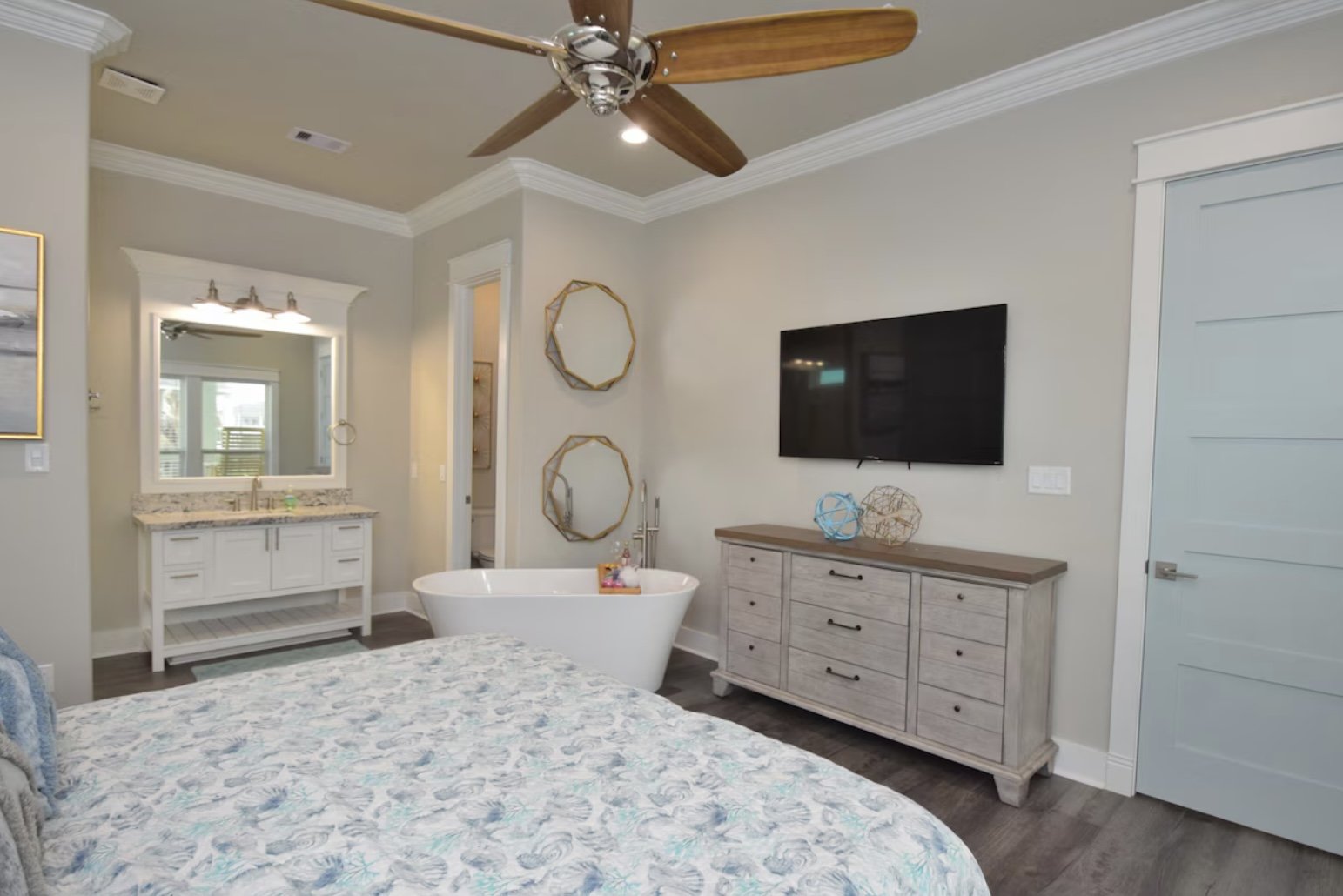Modern bedroom with a bathtub, flat-screen TV, dresser, and decorative mirrors